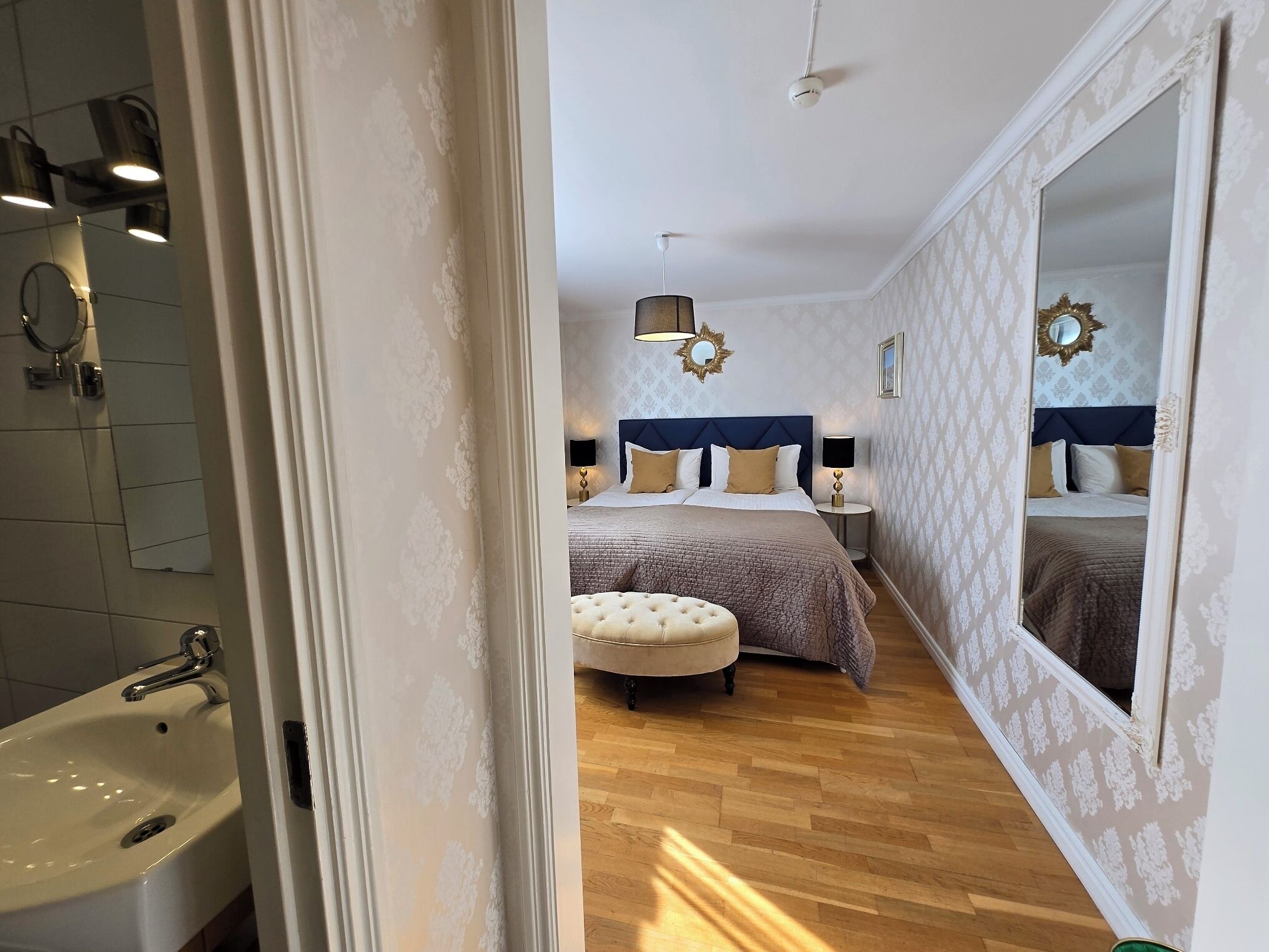 A bedroom with a large bed, a sitting area, and a bathroom with a sink and mirror.