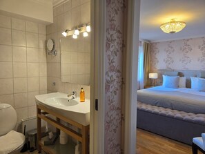 A bathroom with a sink, mirror, and toilet. There is a bed with a headboard and pillows in the adjacent room. - Vänerport Lakefront (Mariestad)