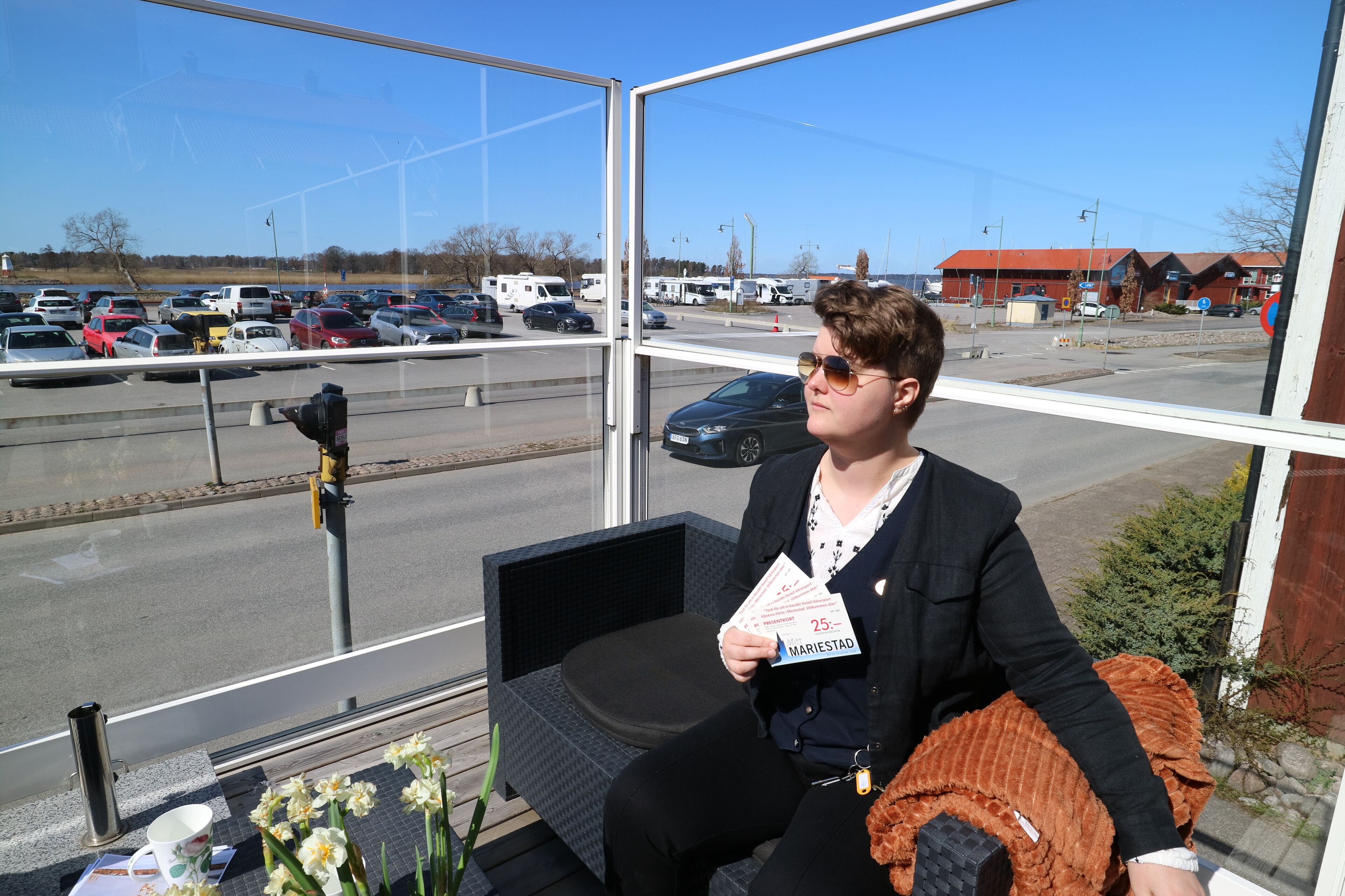 Una persona sentada en un balcón con vista a un estacionamiento y edificios.