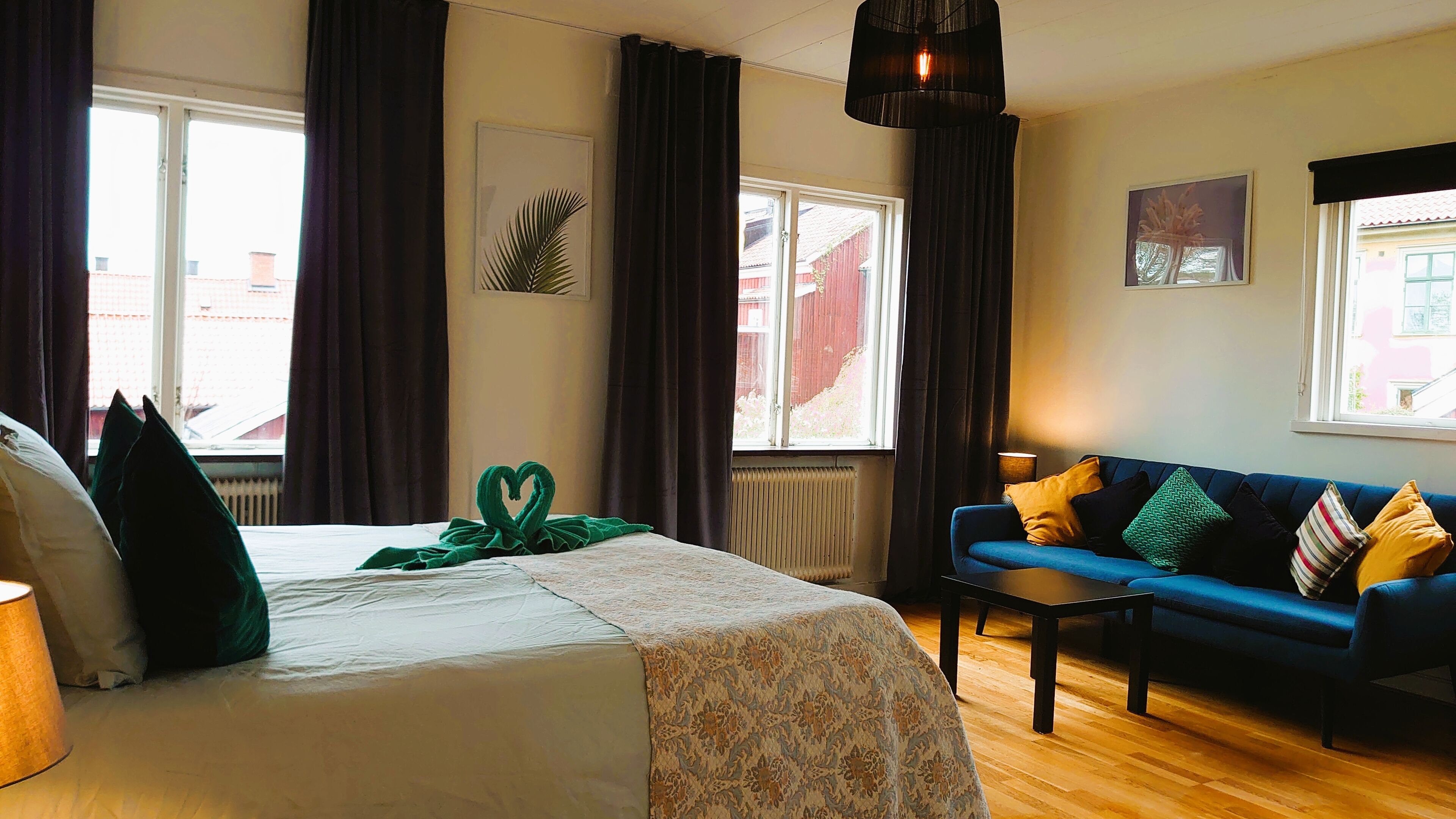 Una habitación de hotel con cama, sofá azul, mesa y ventana con cortinas.