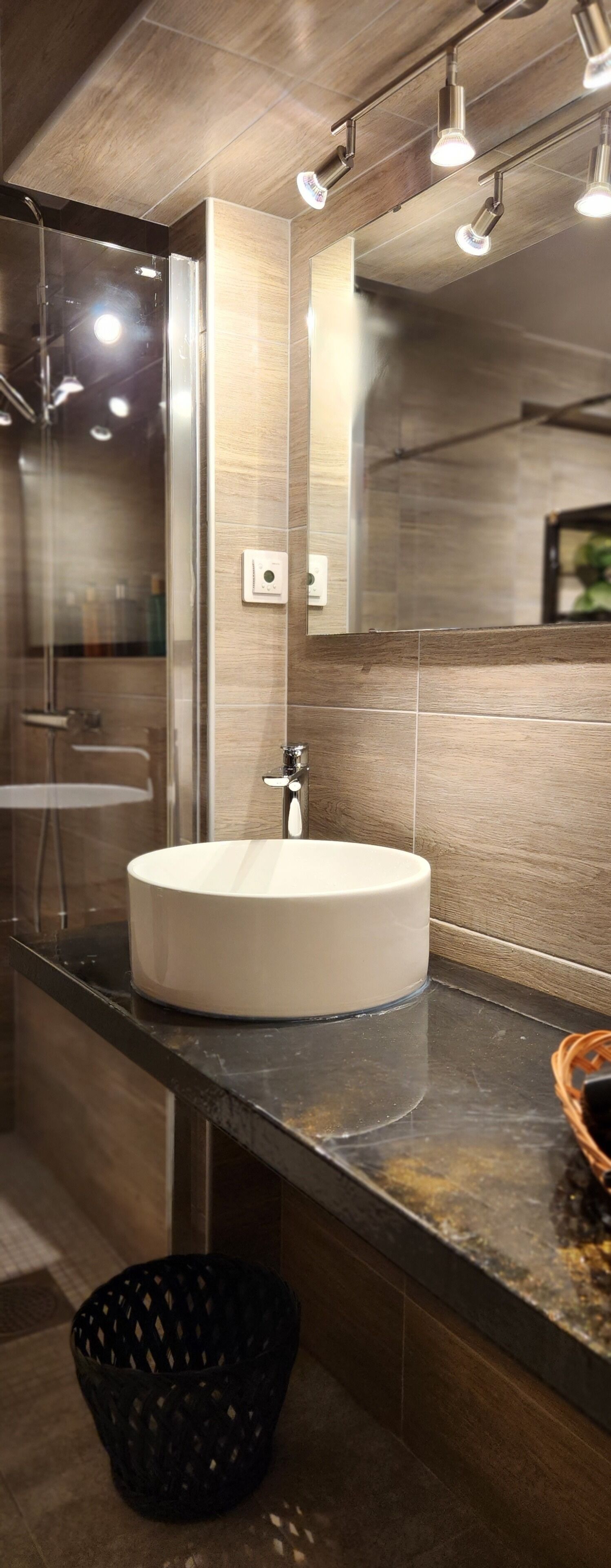 A modern bathroom with a round white sink, a glass shower enclosure, and a large mirror.