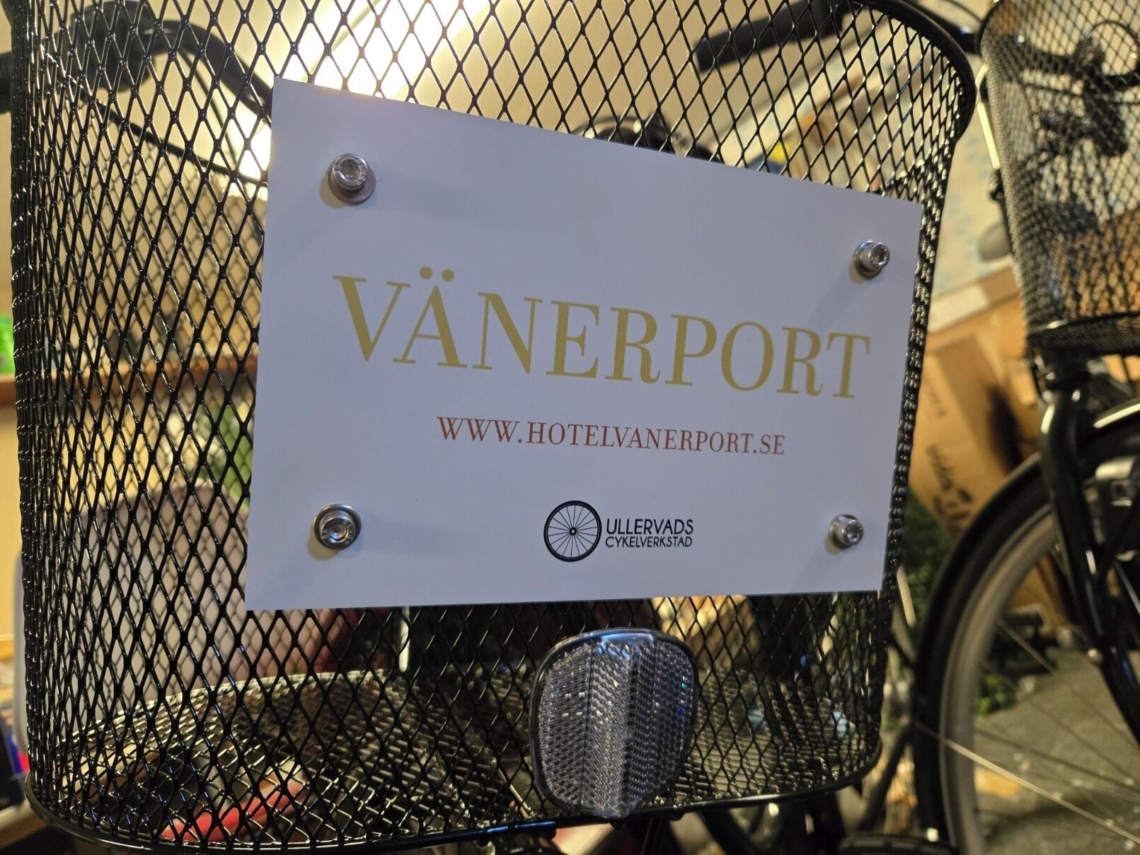 Ein Schild an einem Fahrradkorb mit der Aufschrift 'VÄNERPORT' und einer Website-Adresse.