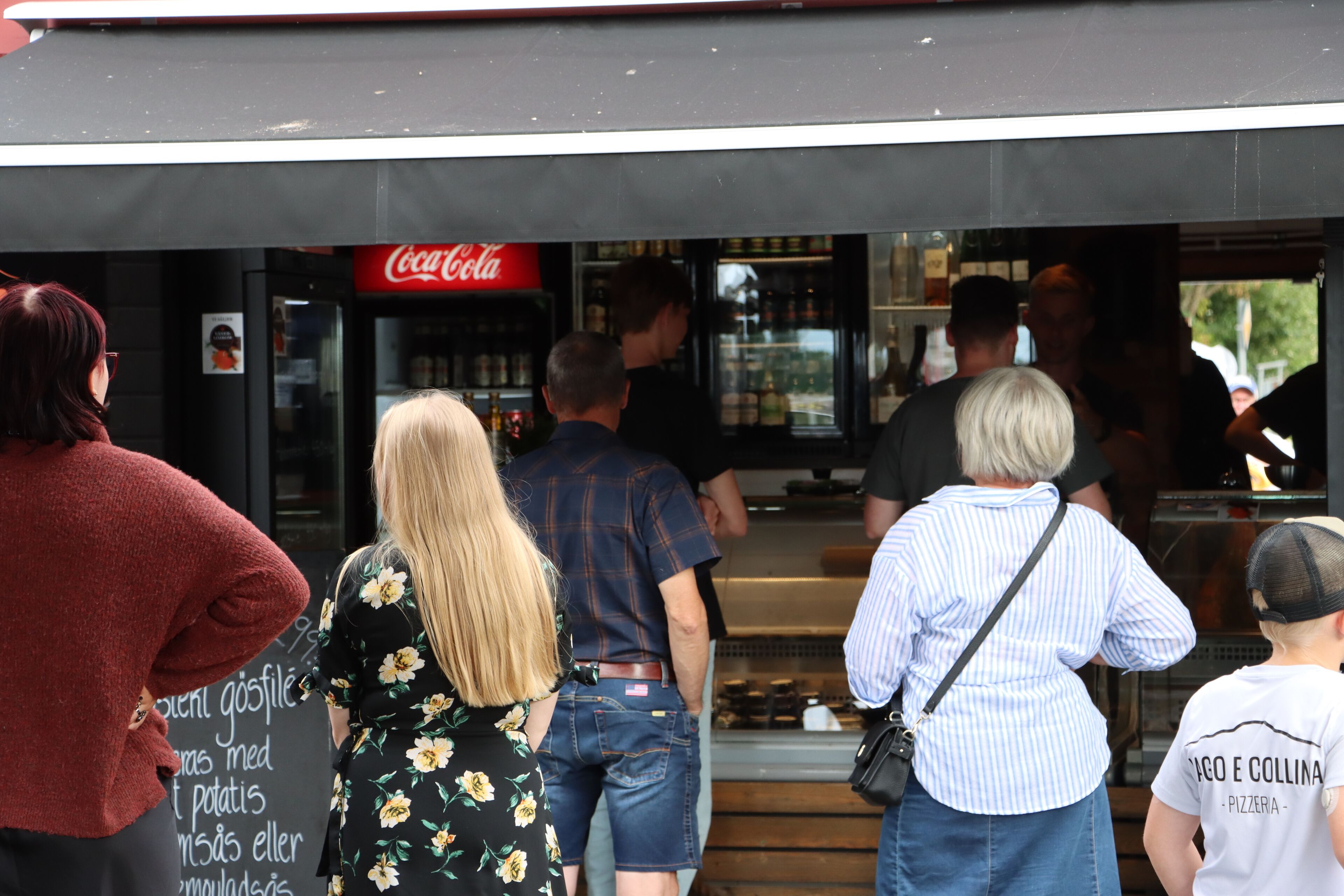 Un groupe de personnes se tient devant un bâtiment sur lequel on peut voir une enseigne Coca-Cola.