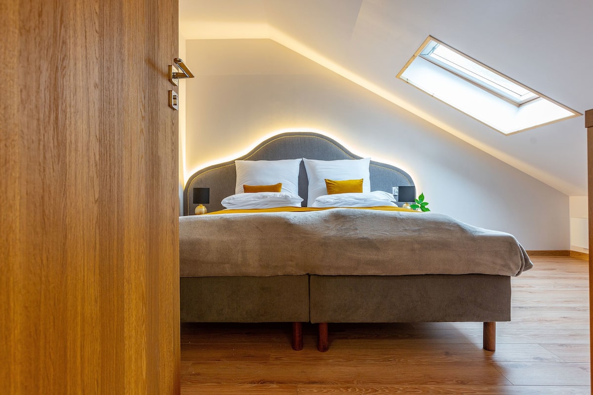 Une chambre avec un plafond en pente, un puits de lumière, un lit avec une tête de lit et un plancher en bois.