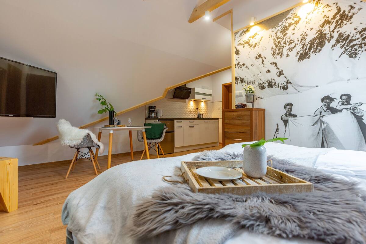 Une chambre confortable aménagée en mezzanine, avec un grand lit, un coin repas et une cuisine.