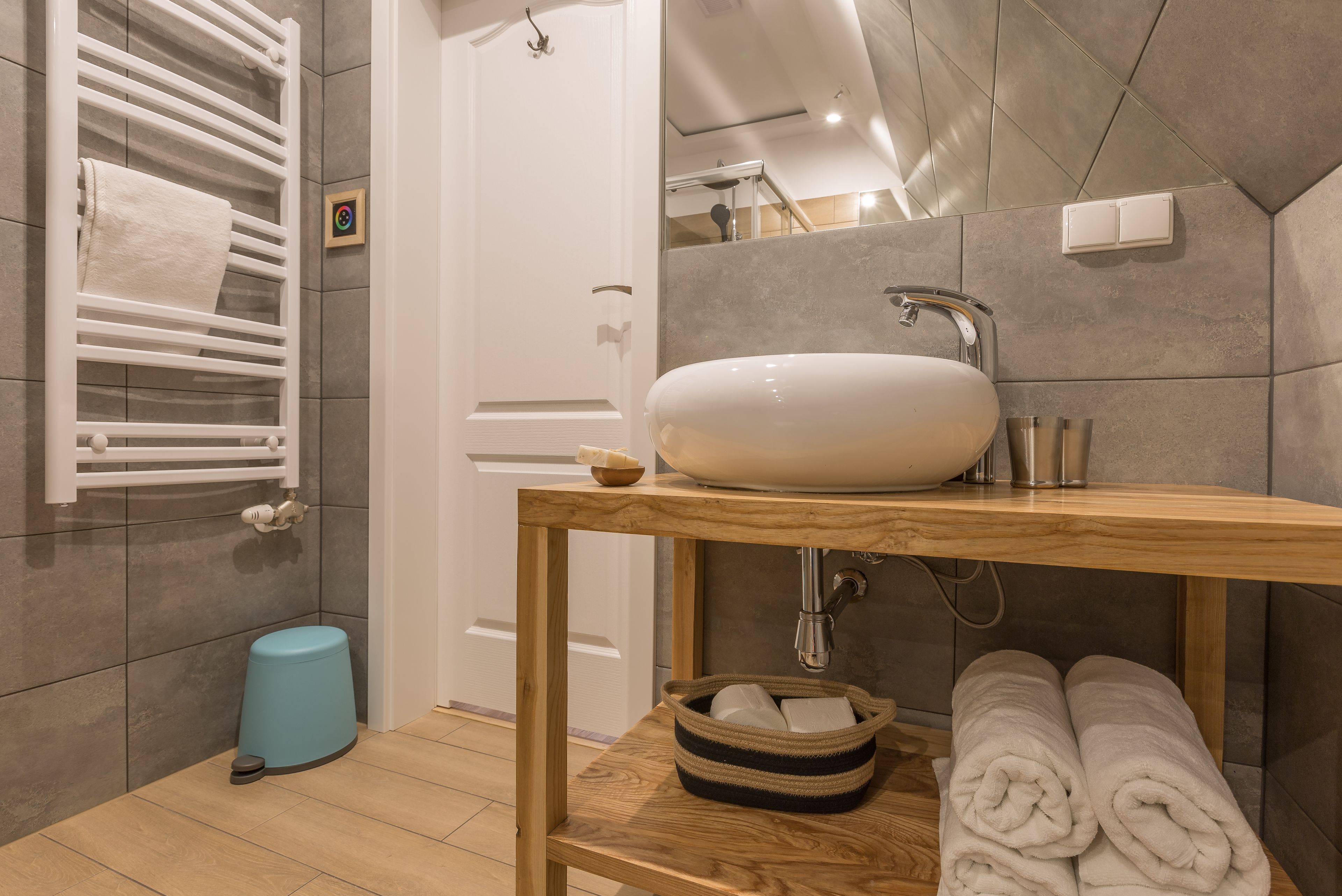 A bathroom with a wooden vanity, a white sink, a towel rack, and a blue trash bin.