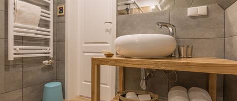 A bathroom with a wooden vanity, a white sink, a towel rack, and a blue trash bin.