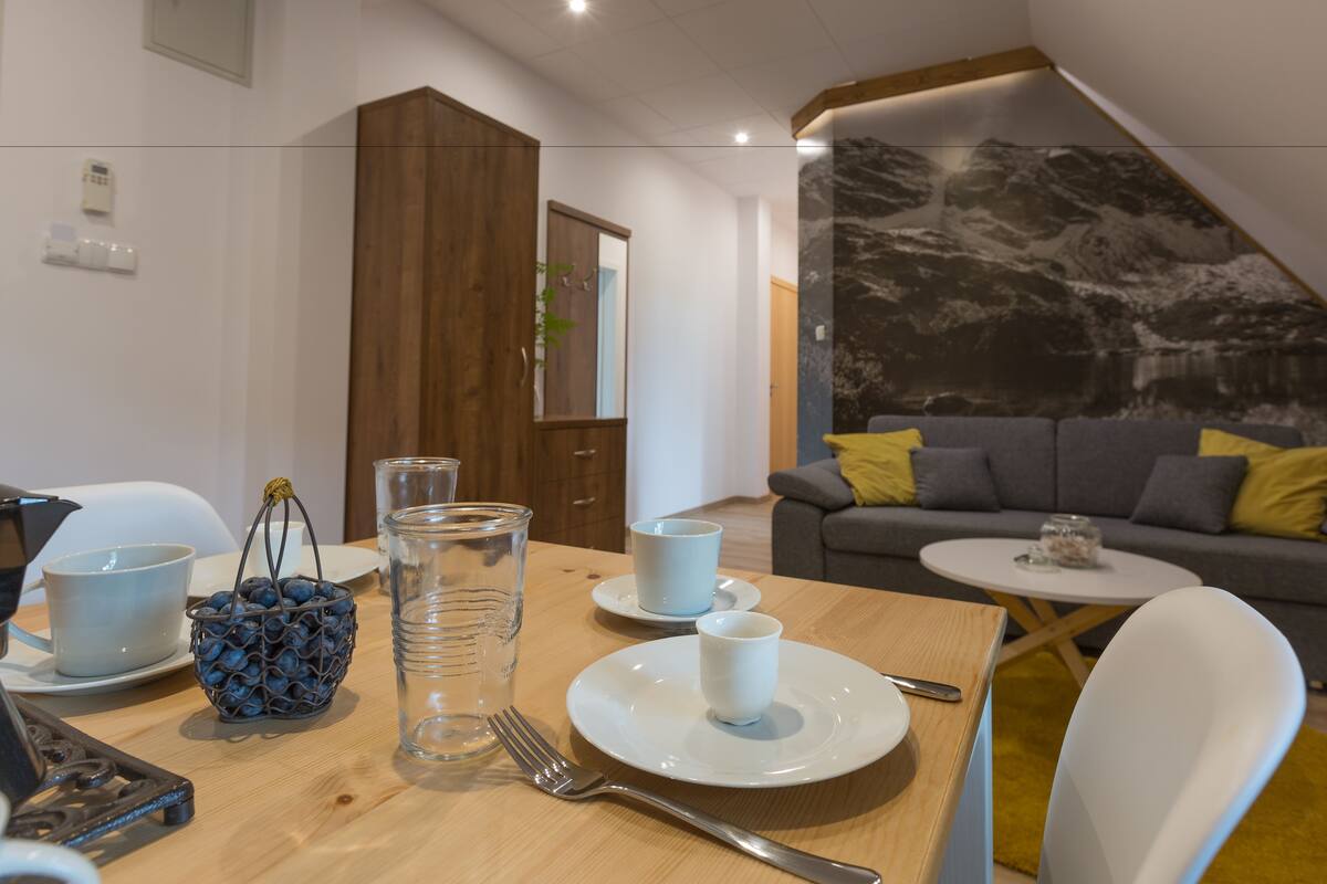 Un coin repas avec une table en bois dressée pour deux personnes, un canapé et une petite table ronde avec un verre.