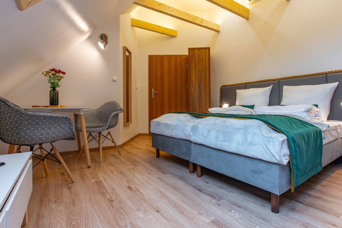 Une chambre à coucher comprenant un lit, une table de chevet, une lampe, une chaise et une petite table sur laquelle est posé un vase.