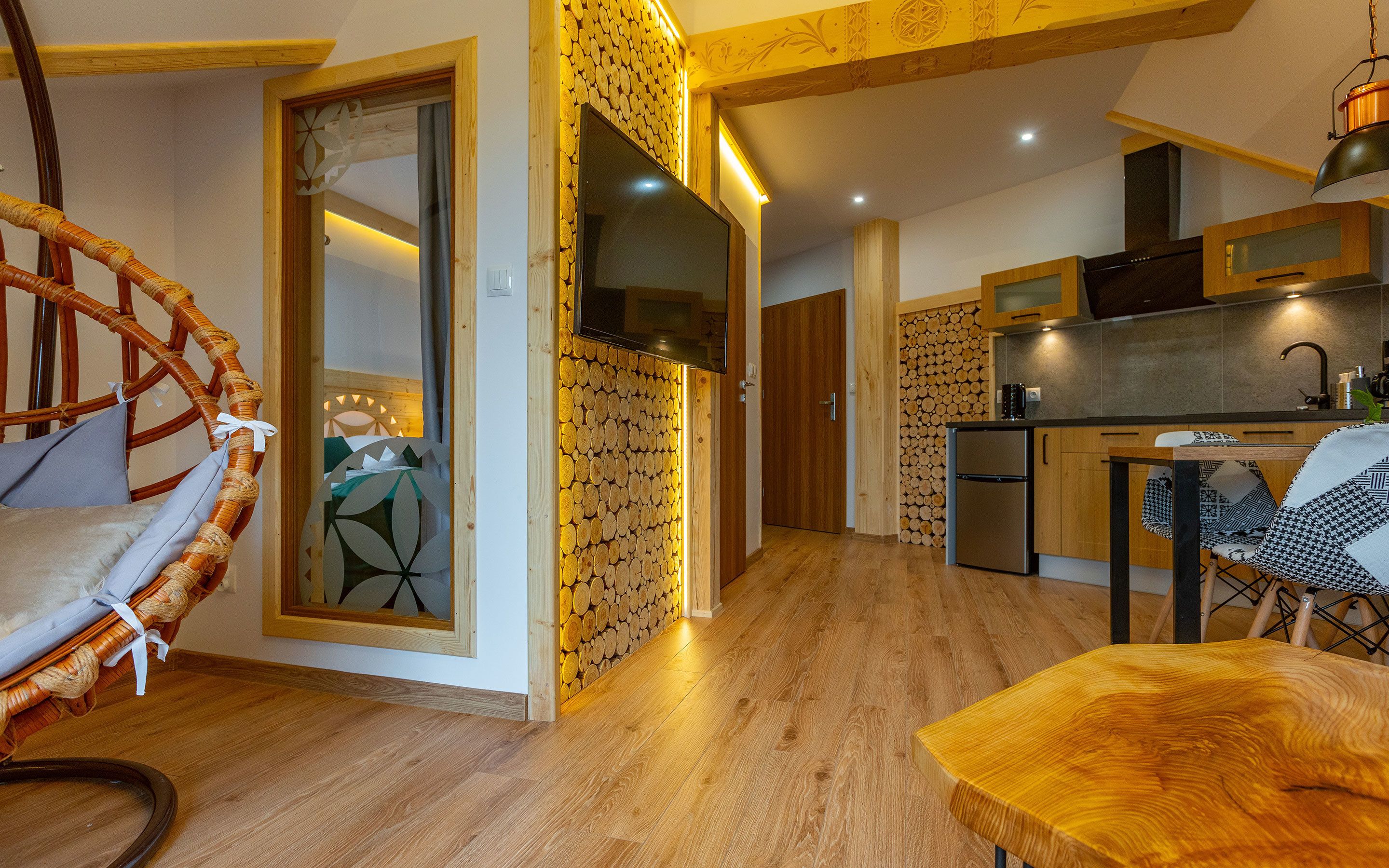 A modern kitchen with wooden cabinets, a refrigerator, and a dining area with a wooden table and chairs.
