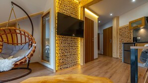 Un intérieur moderne avec un fauteuil suspendu, un mur recouvert de bûches empilées et un coin cuisine.