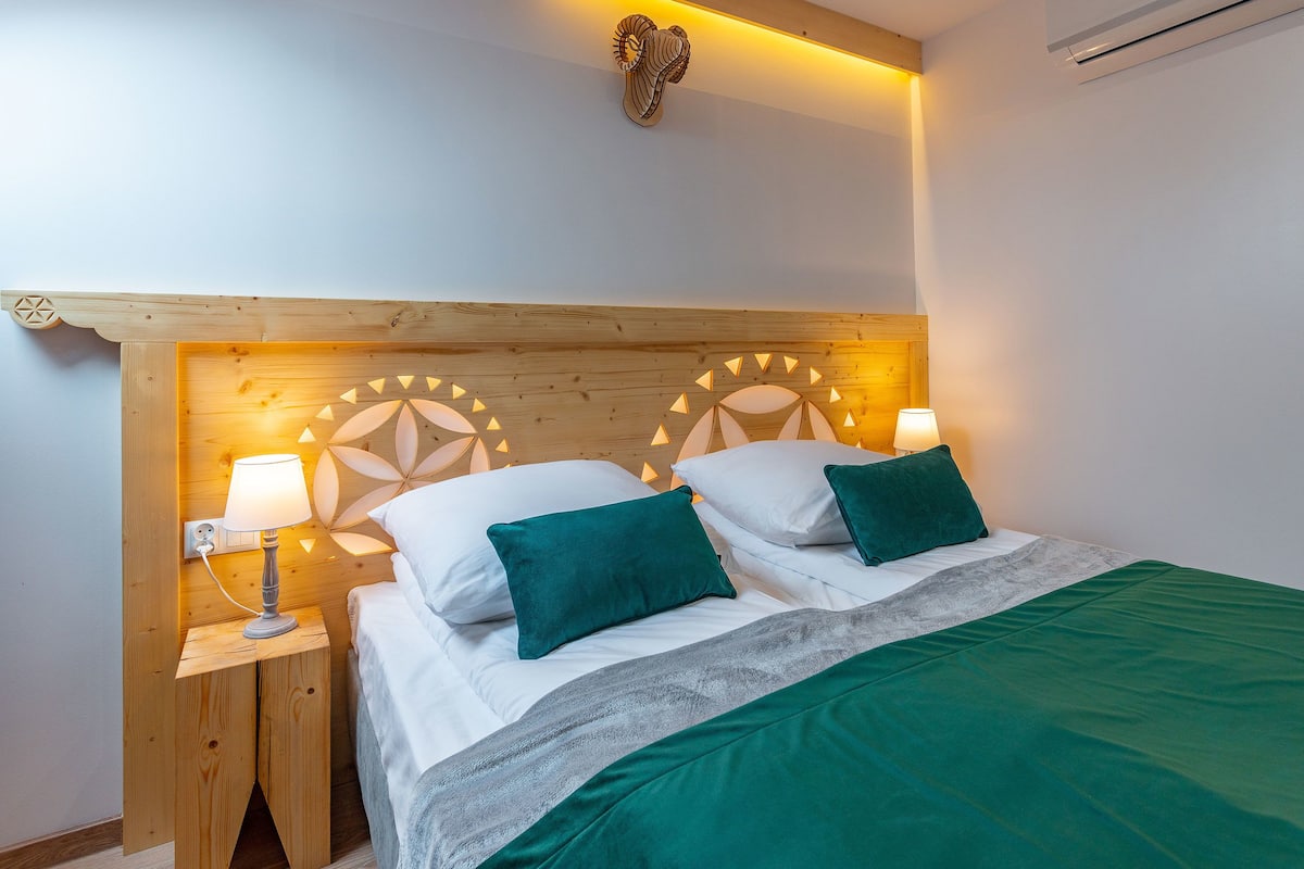 Une chambre à coucher avec une tête de lit en bois, deux lampes de chevet et un plaid vert.