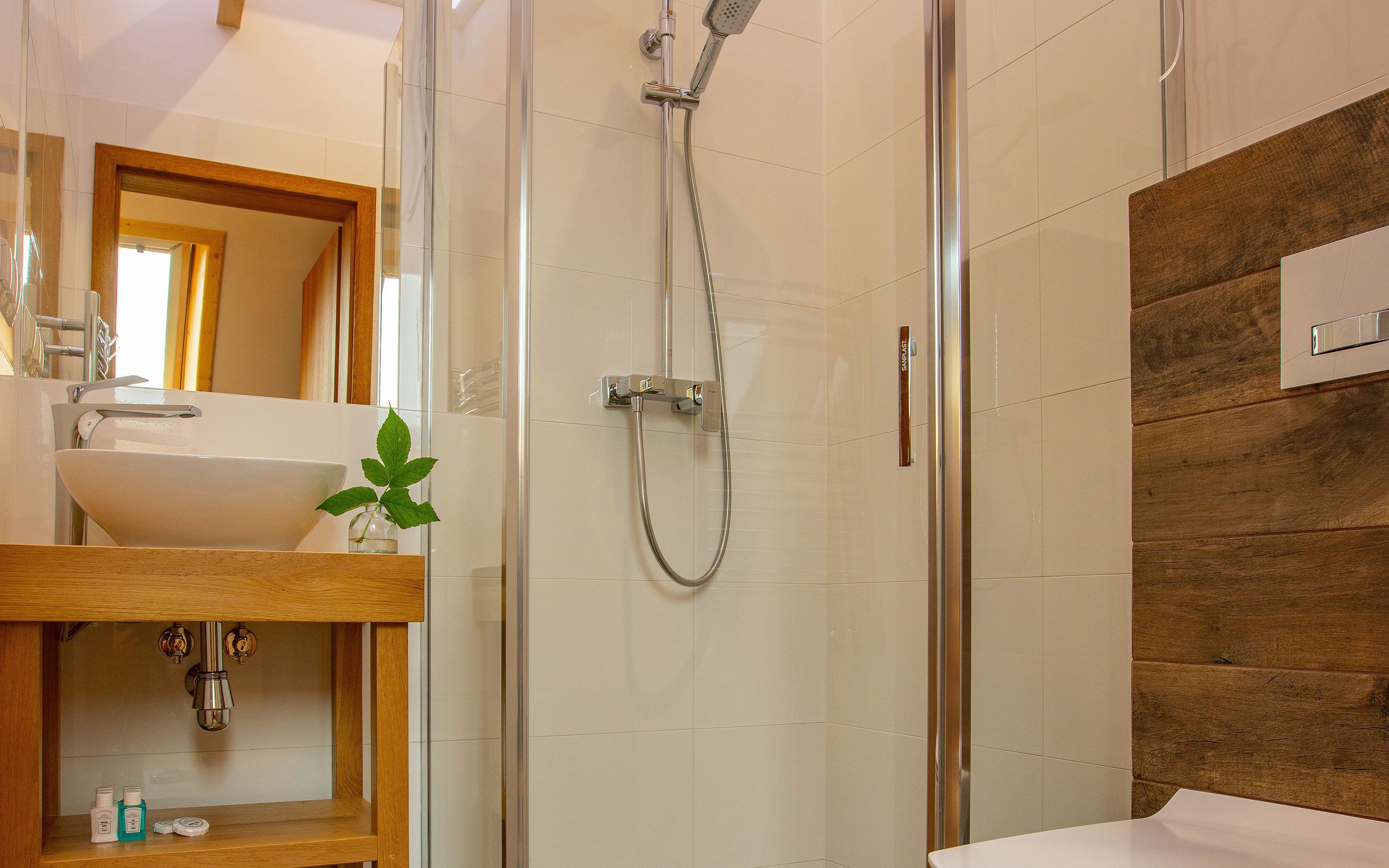 A modern bathroom with a glass-enclosed shower, a wooden vanity with a sink, and a mirror.
