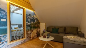 Une pièce chaleureuse avec un plancher en bois, une table ronde, un canapé et une fresque représentant un paysage de montagne.