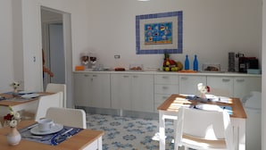 A bright kitchen with white cabinets, a tiled backsplash, and a wooden dining table with chairs. - B&B Riva delle Donne (Taviano)