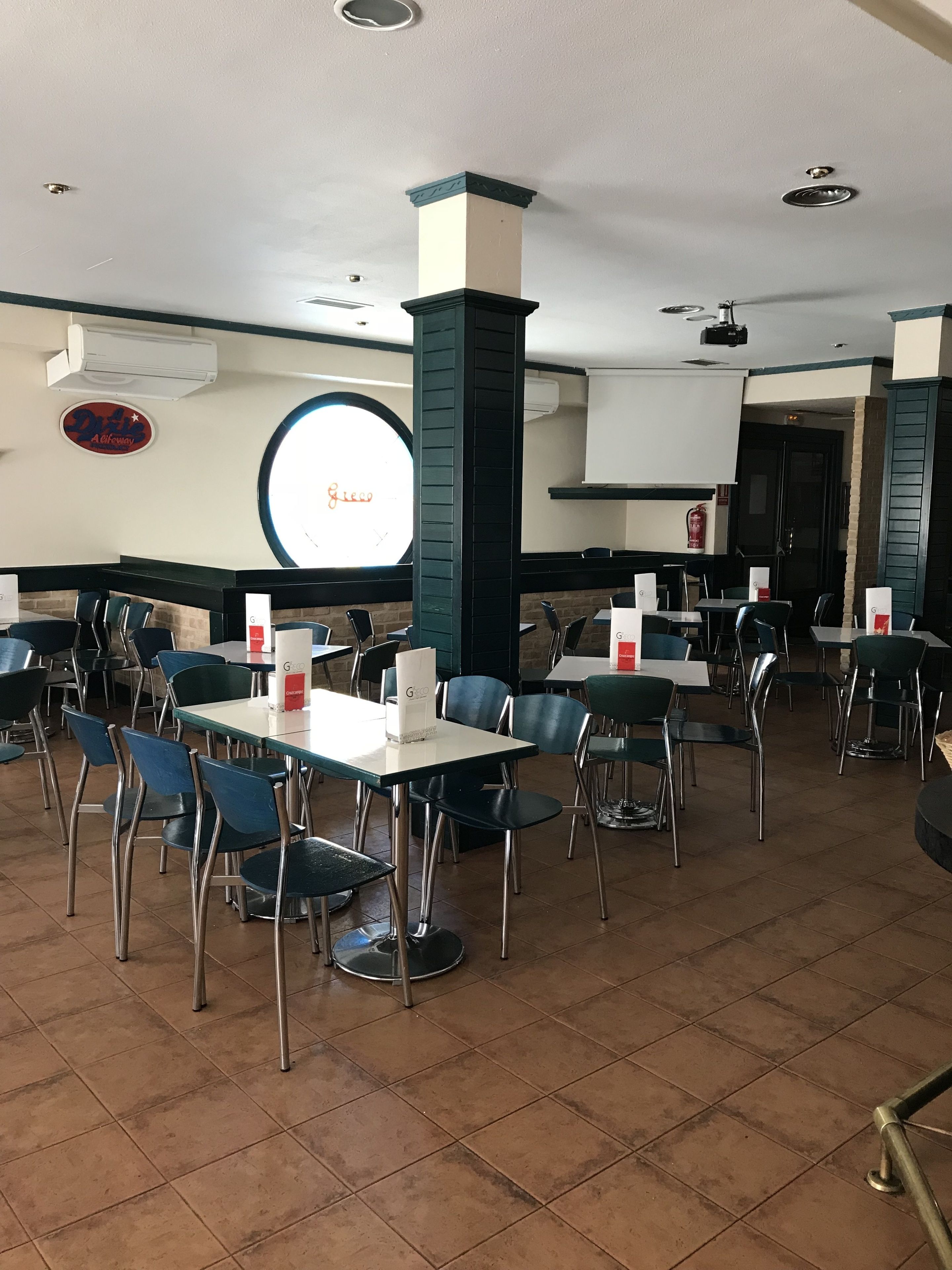 En restaurant med flere borde og stole, et rundt vindue og et skilt på væggen.