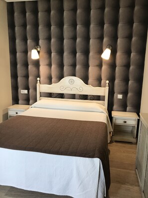 A bedroom with a tufted headboard, a bed with a white and brown bedspread, two bedside tables with lamps, and a nightstand with a drawer. - Hostal Cafe Gutgreco (Sonseca)