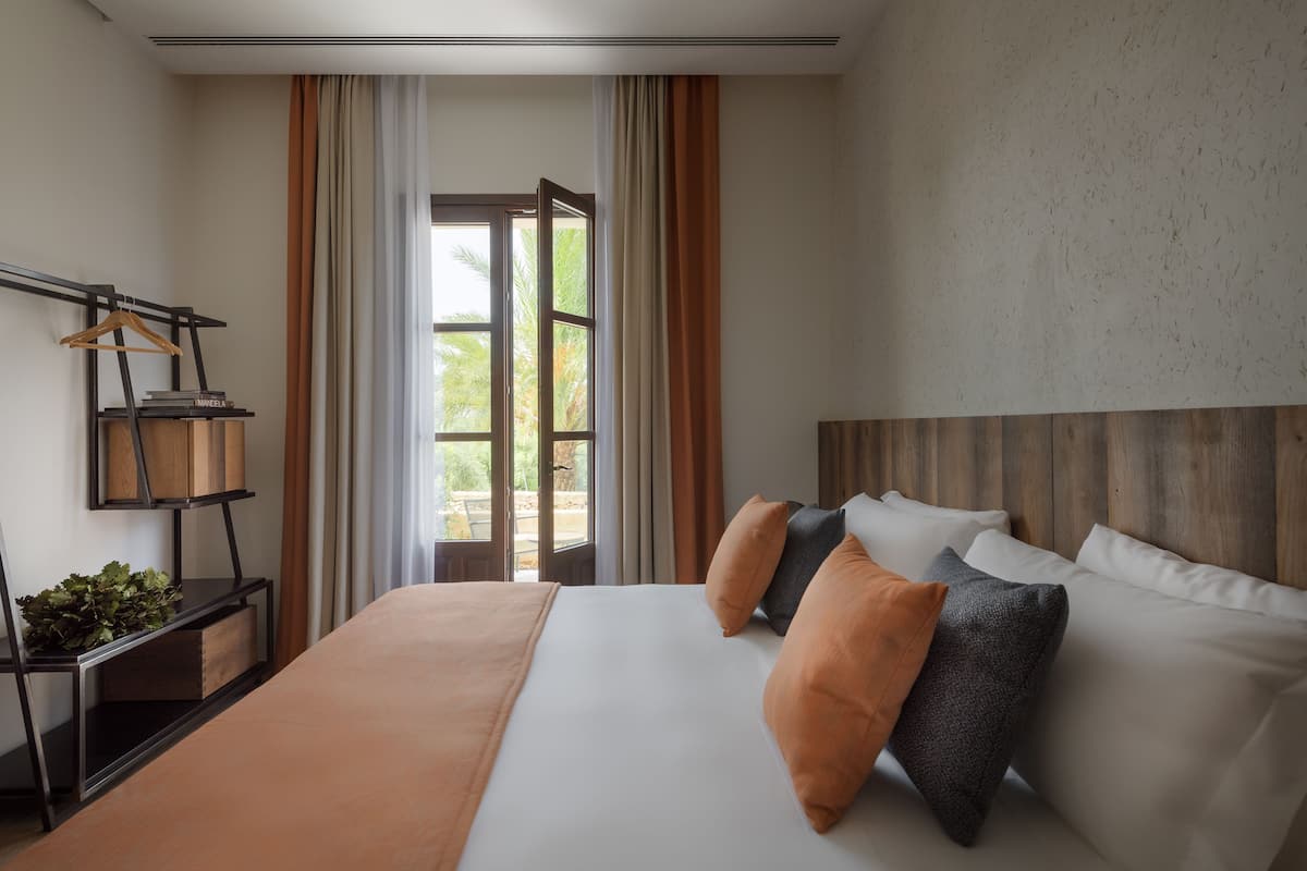 A hotel room with a large bed, a wooden headboard, and a view through an open door to the outdoors.