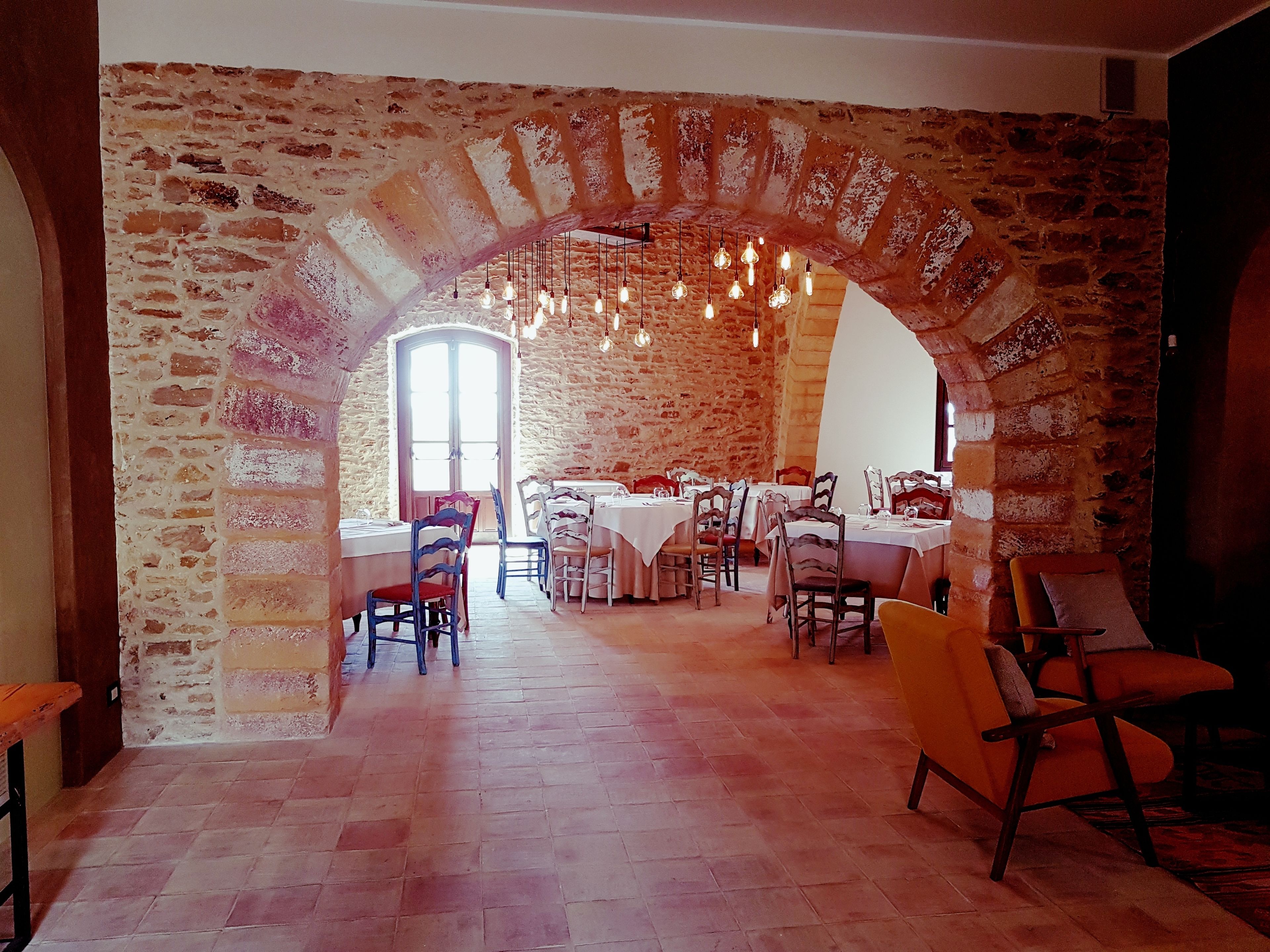 Un comedor con paredes de ladrillo, techo alto y lámparas colgantes. Las mesas están cubiertas con manteles blancos y sillas.