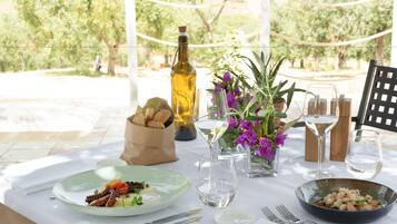 Mesa al aire libre para dos personas, con platos de comida, copas de vino y una botella de aceite de oliva.