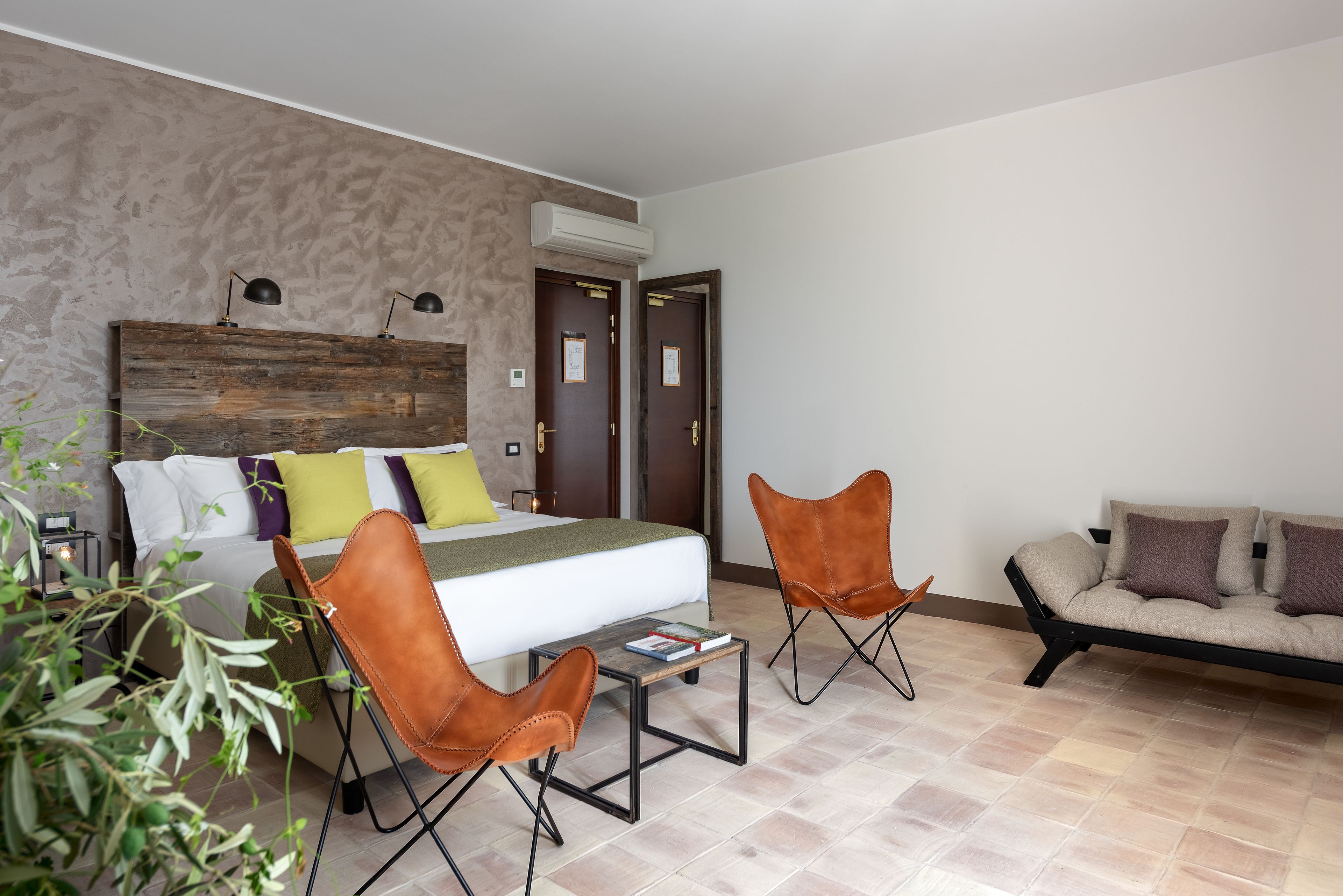 A hotel room with a bed, two brown leather chairs, a sofa, a small table, and a large wooden headboard.