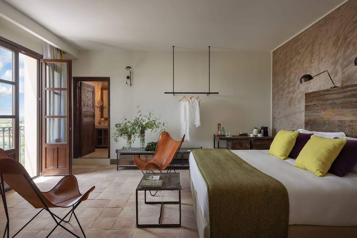 A modern bedroom with a large bed, a desk, a chair, and a view of the outdoors.