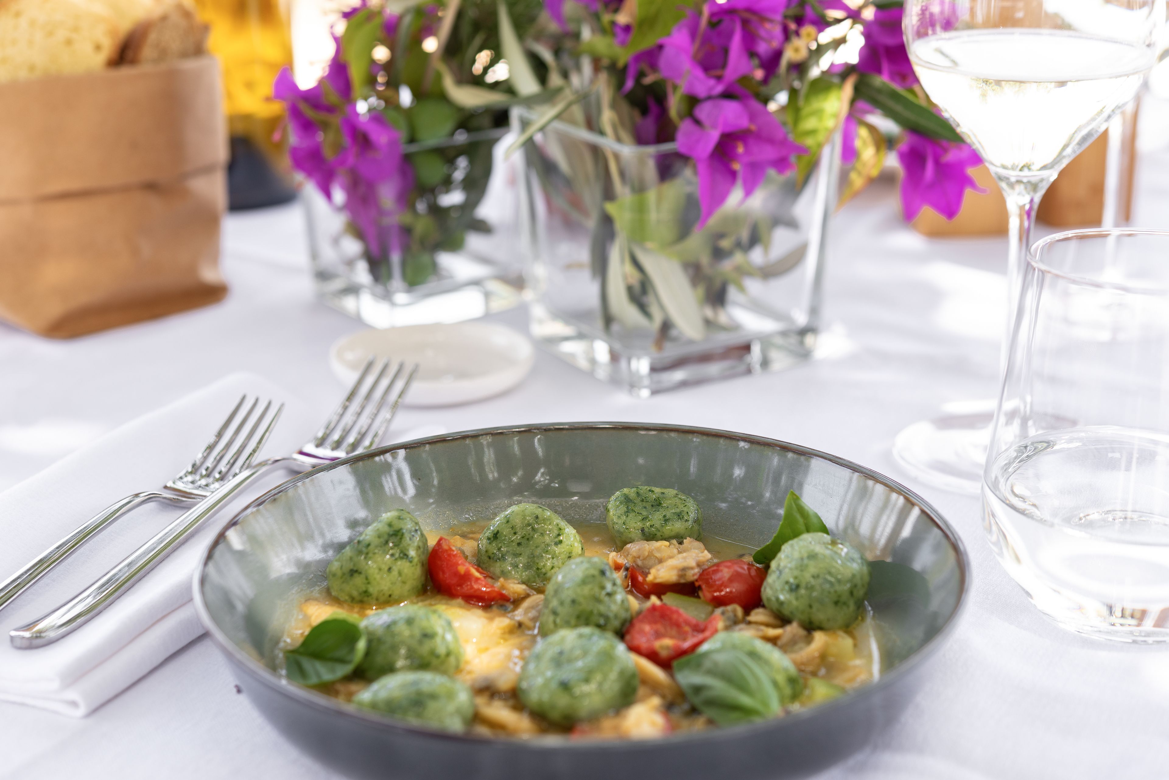 A dining table with a bowl of food, a glass of water, and a vase of flowers.