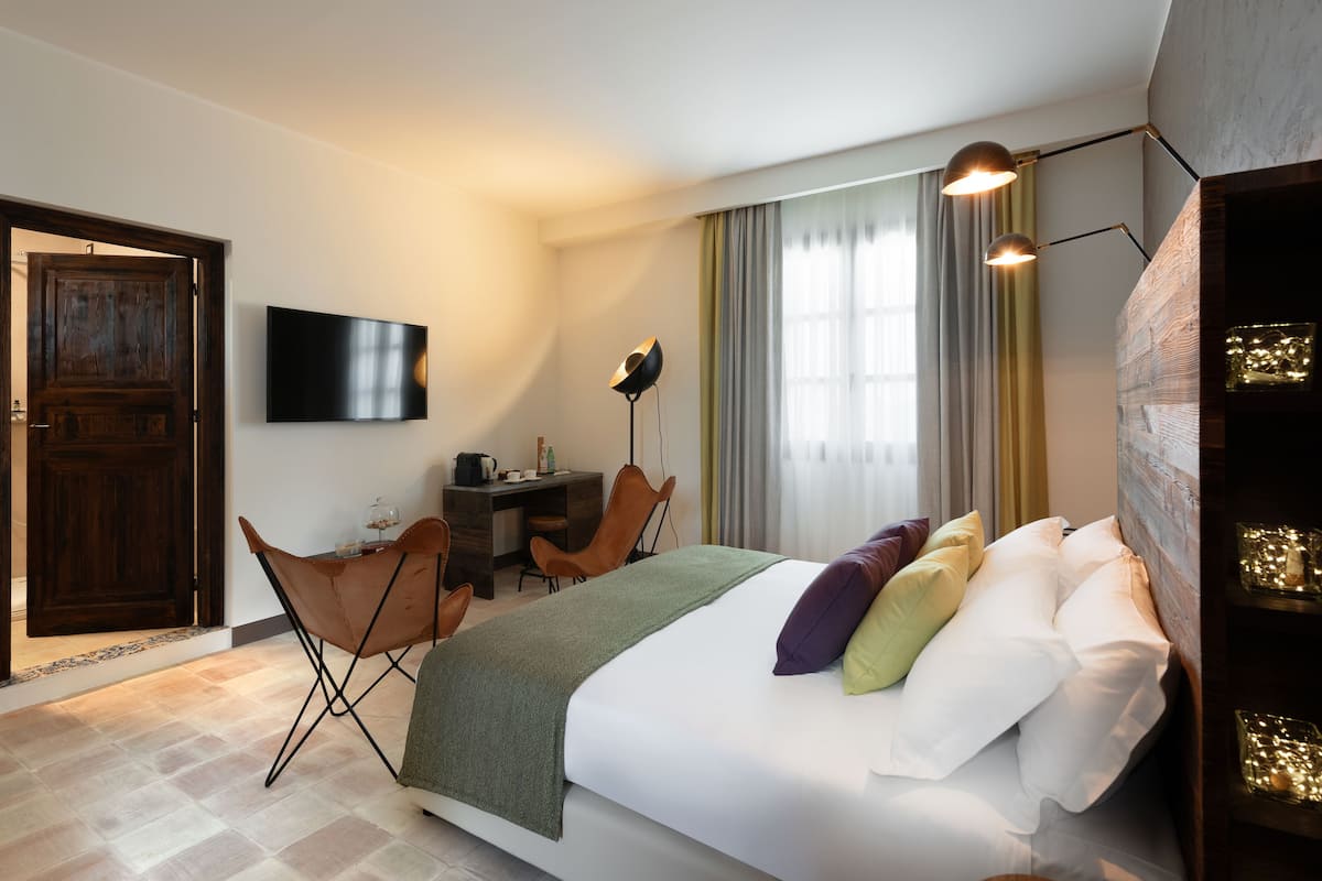 A hotel room with a bed, a desk, a chair, a TV, and a window with curtains.