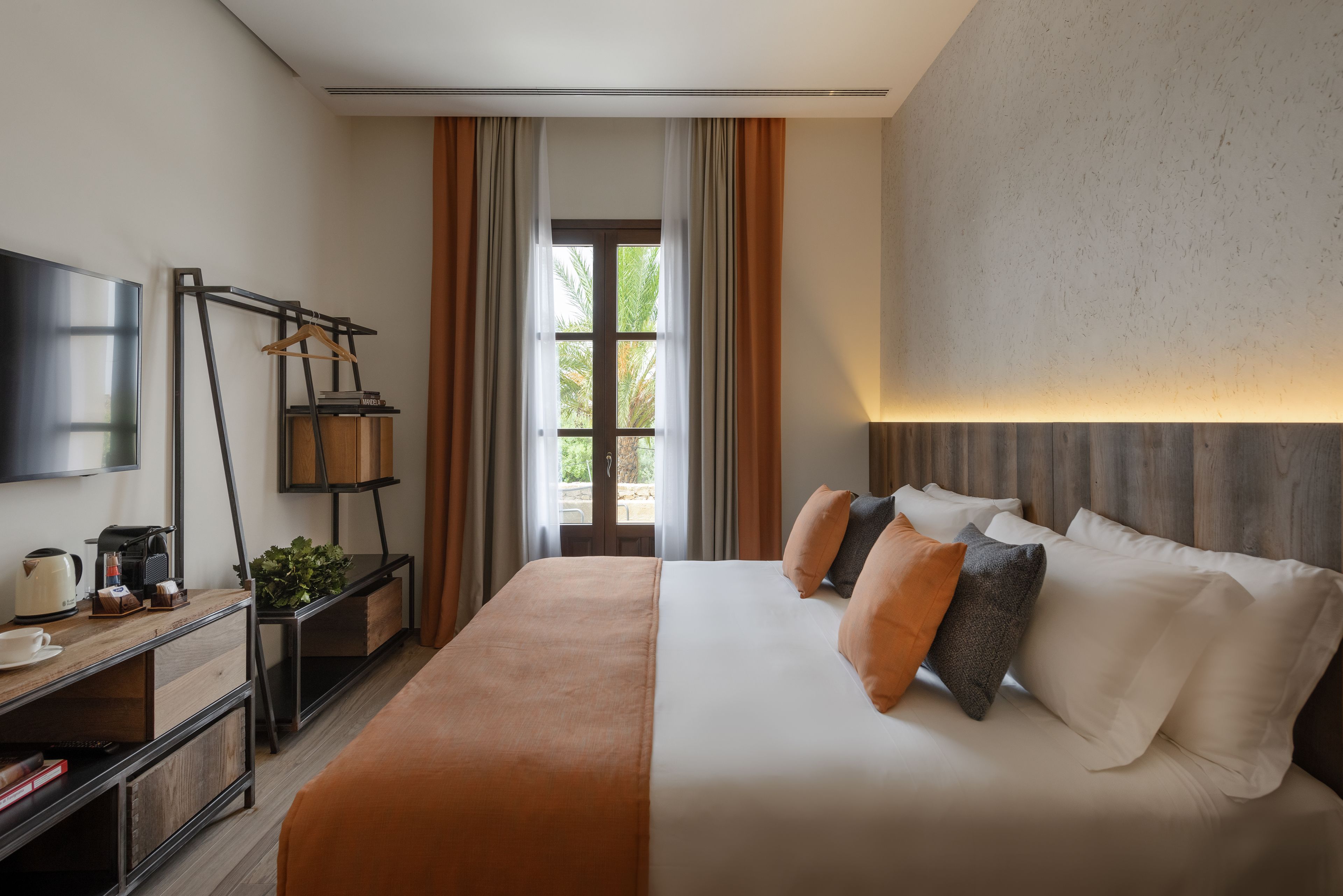 A hotel room with a bed, a desk with a coffee maker, a TV, and a window with curtains.
