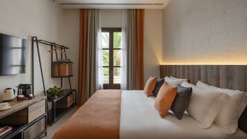 A hotel room with a bed, a desk with a coffee maker, a TV, and a window with curtains.