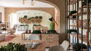 Una sala de estar moderna con una mesa de centro de madera, dos sillones blancos, una estantería y diversas plantas.