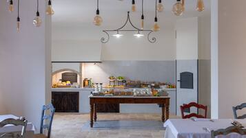 Comedor con una mesa dispuesta para dos, una araña y una cocina al fondo.