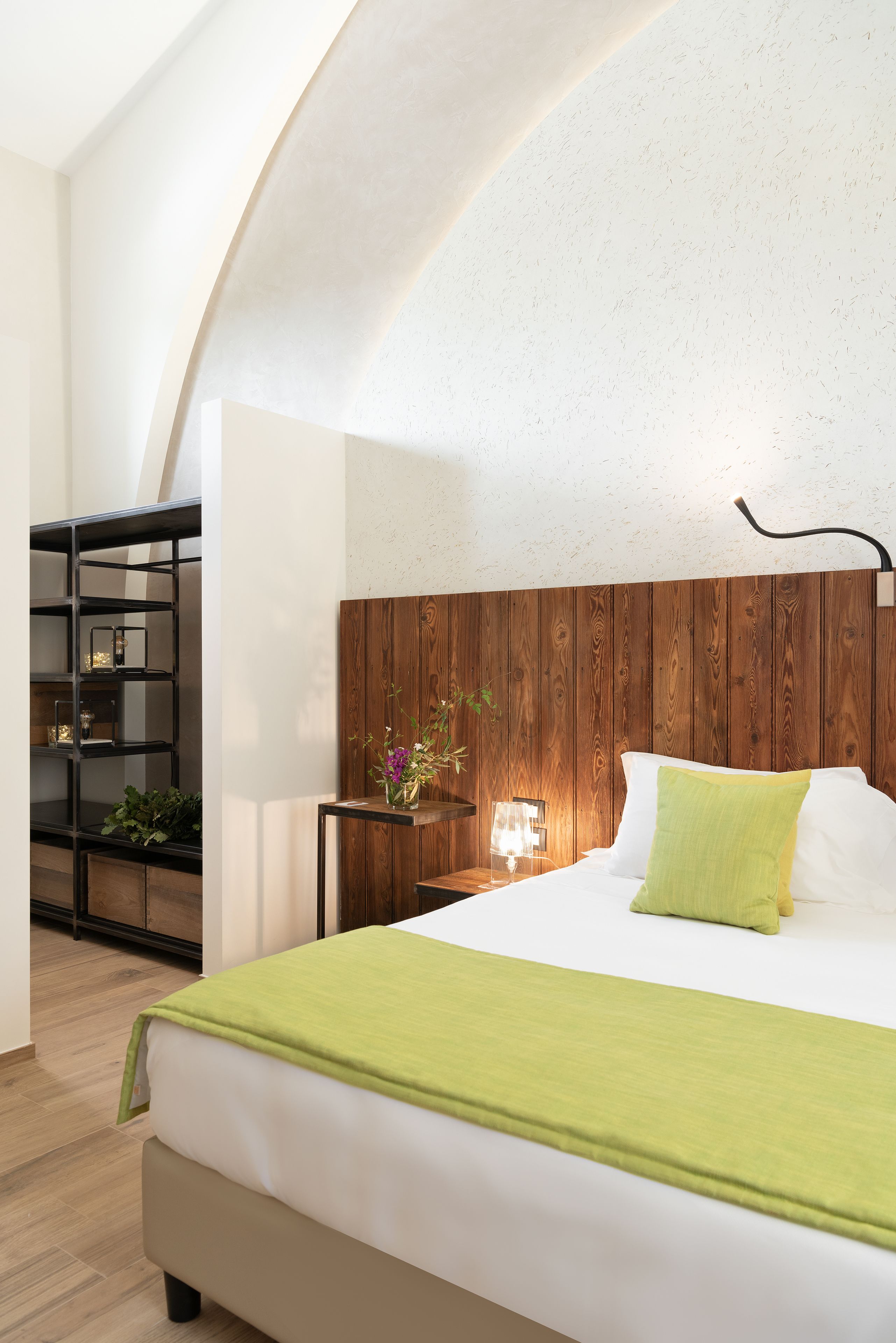 A modern bedroom with a wooden headboard, a green throw blanket, and a bedside table with a lamp.