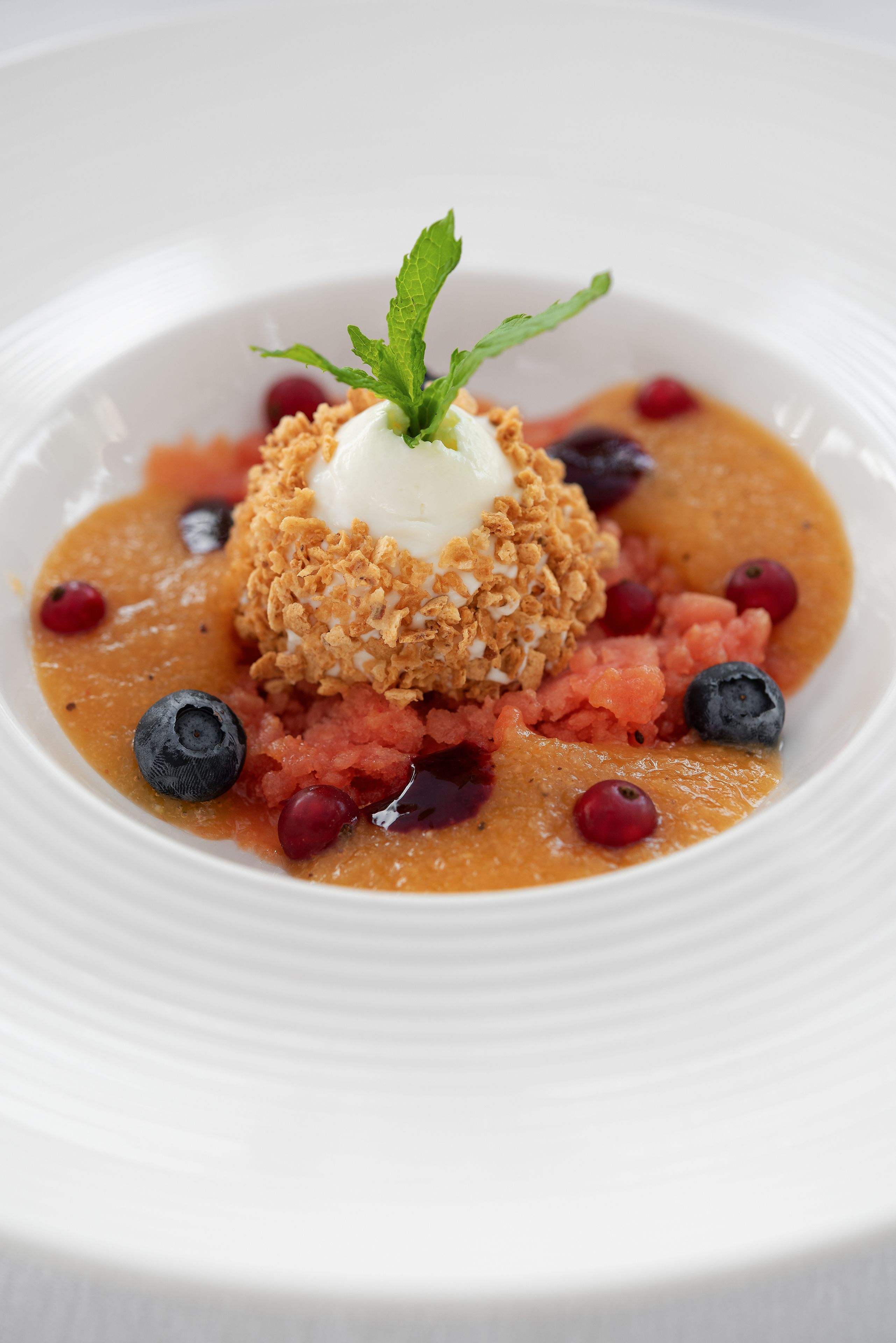 Un plato blanco con un postre hecho de un montón de cereal desmenuzado, una bola de helado y una guarnición de hojas de menta.