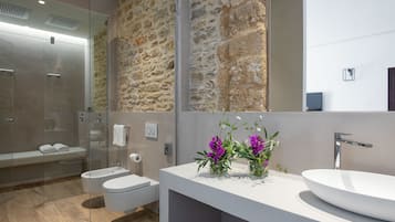 Een moderne badkamer met een stenen muur, een douche met glazen wanden, een wit wastafelmeubel en een toilet.