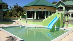 Une piscine avec un toboggan, entourée de bâtiments dotés de toits végétalisés et d’une bouée de sauvetage placée au bord de la piscine.
