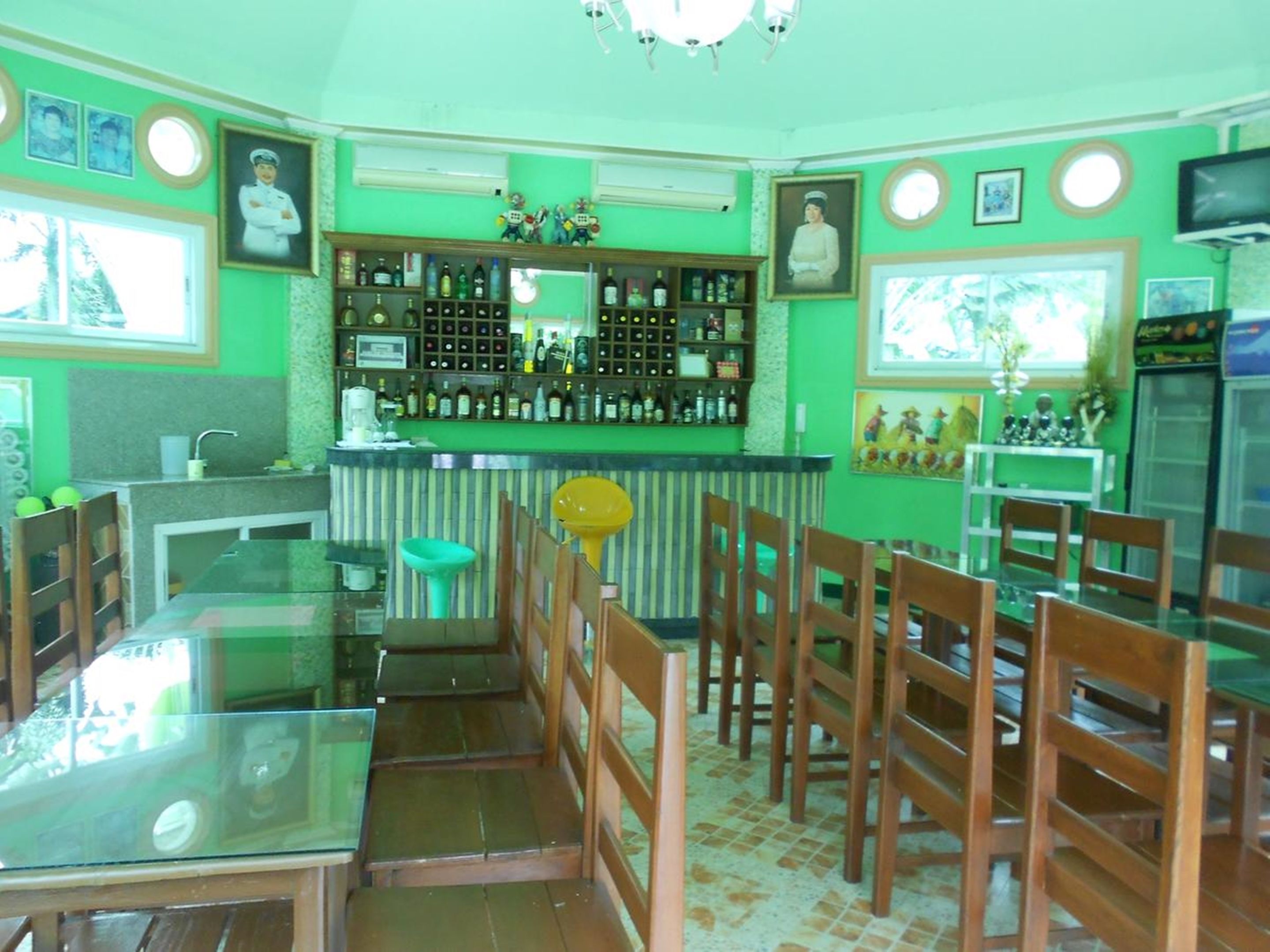 A bar area with a counter, shelves of bottles, and a seating area with wooden chairs and a glass table.