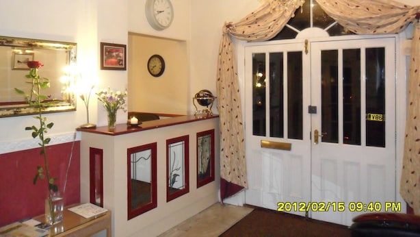 A reception area with a reception desk, a clock, a mirror, and a door with a curtain. - Thorpe Lodge Hotel (Peterborough)