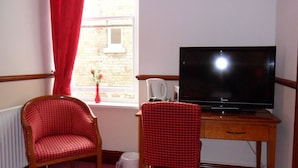A room with a television on a wooden stand, a red checkered chair, and a window with a red curtain. - Thorpe Lodge Hotel (Peterborough)