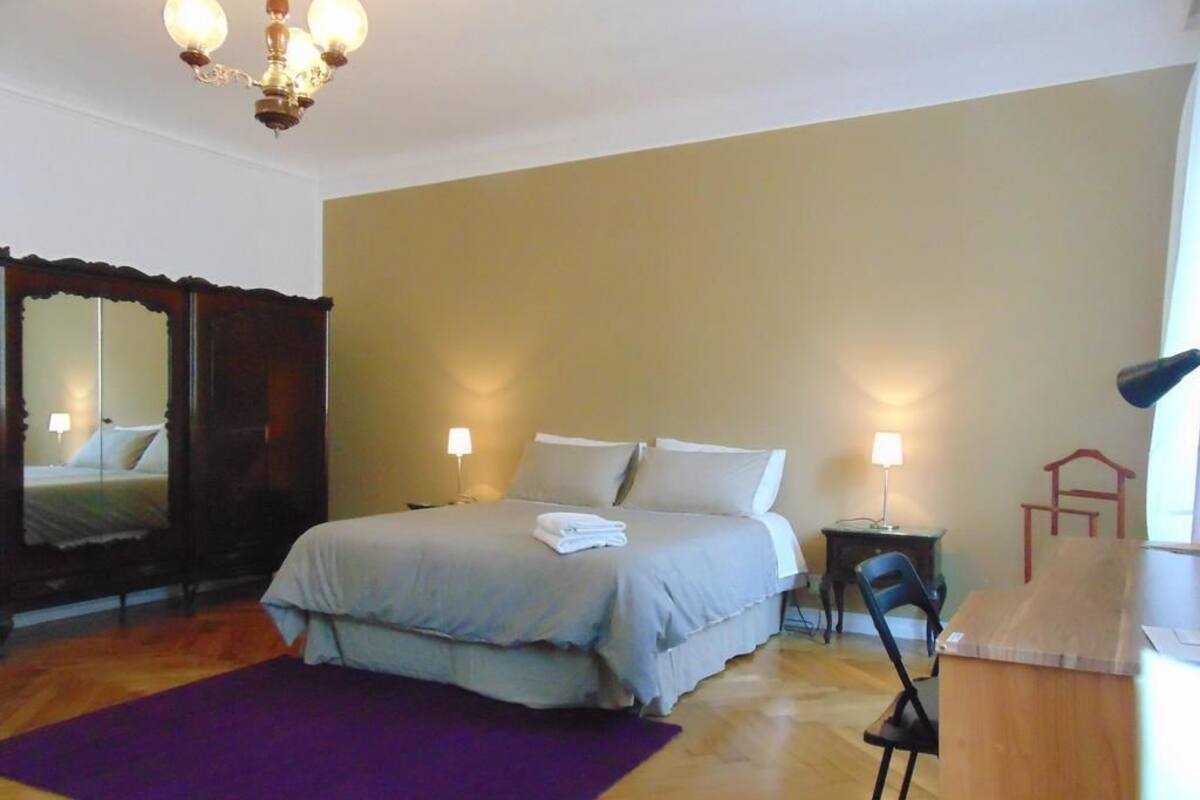 Un dormitorio con cama, dos mesitas de noche, una silla, un escritorio, un espejo y una araña.