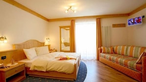 A hotel room with a bed, a sofa, a TV, and a mirror. - Pra Fiorì (Mazzin)