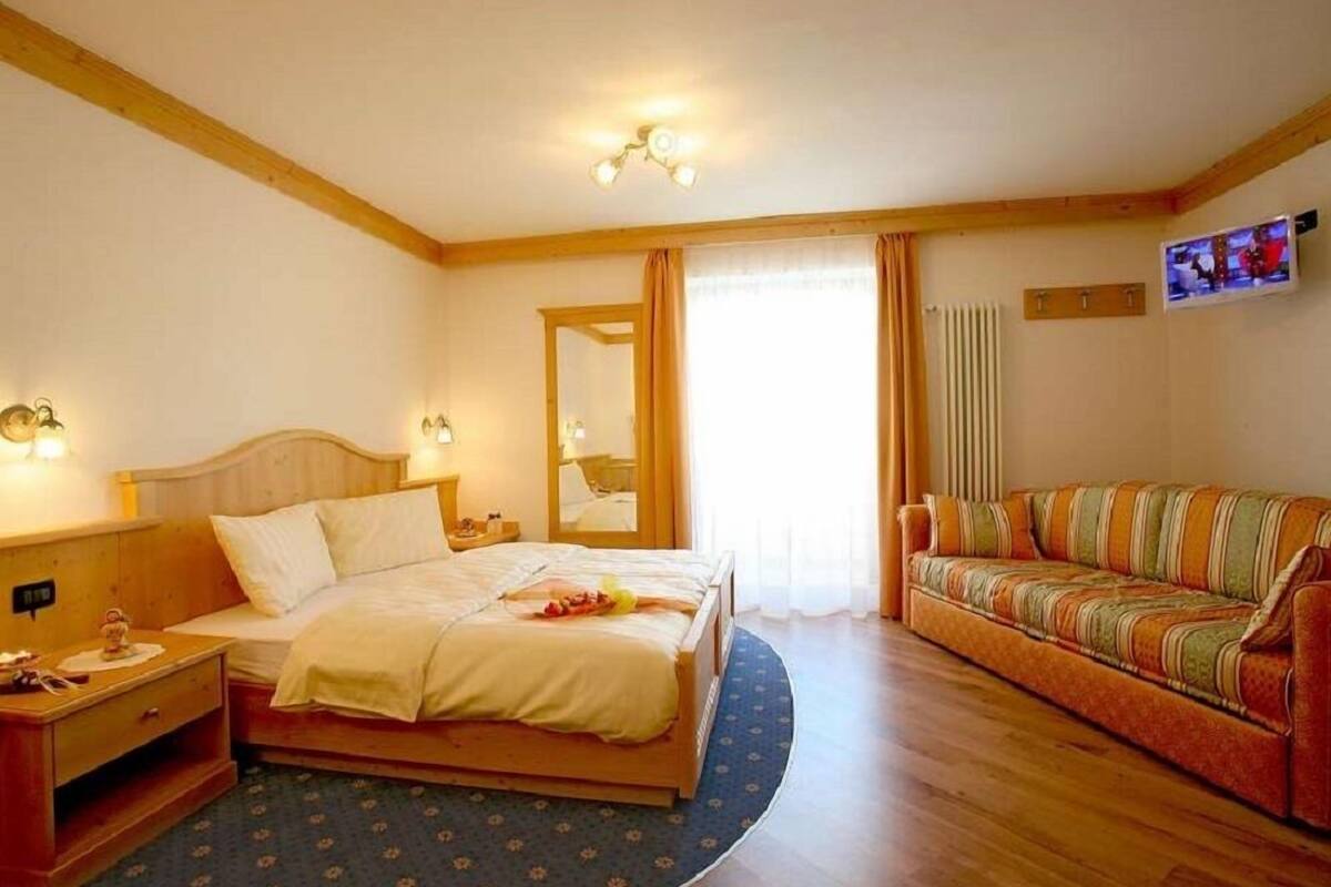 Hotellihuone, jossa on sänky, sohva, televisio ja peili.