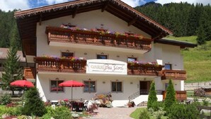 A two-story building with balconies adorned with flowers, a sign reading "Garnier Pasztor," and outdoor seating with red umbrellas. - Pra Fiorì (Mazzin)