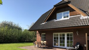 A two-story house with a tiled roof, a brick exterior, and a covered patio with outdoor furniture.