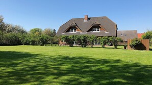 A large house with a sloped roof, surrounded by a well-maintained lawn and trees.