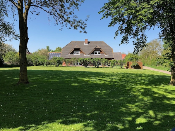 A large house with a sloped roof and solar panels, surrounded by a well-maintained lawn and trees.