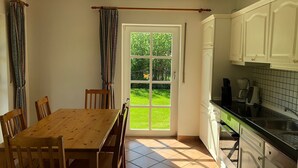 A kitchen with white cabinets, a black countertop, and a view of a green garden through a glass door.
