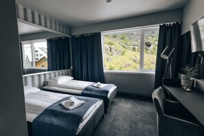 A hotel room with two single beds, a desk with a lamp, a TV, and a window with curtains. - Live Lofoten Hotel (Vestvågøy)