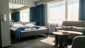 Una habitación de hotel con cama, sofá, una mesita y una ventana con cortinas.