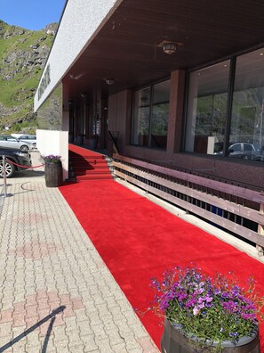 A hotel entrance with a red carpet, steps leading to a covered area, and a mountain backdrop. - Live Lofoten Hotel (Vestvågøy)
